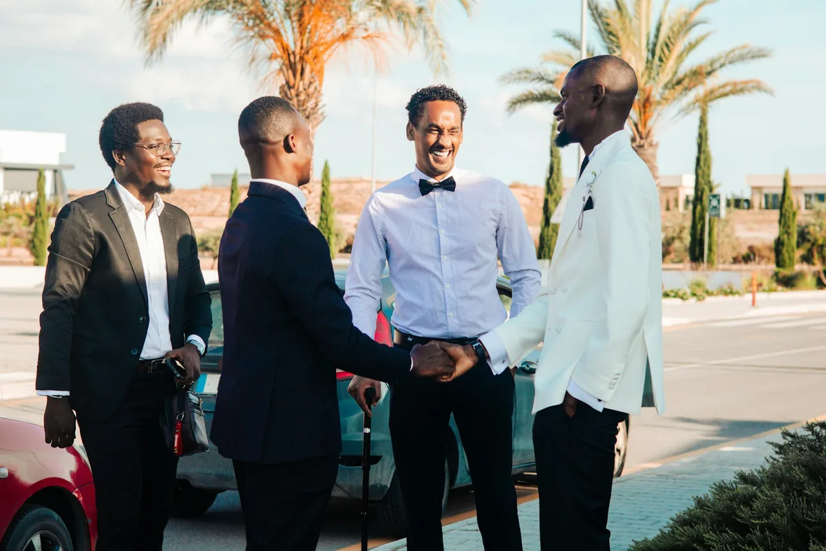 Quatre hommes en tenue de soirée qui se serrent la main, devant des palmiers