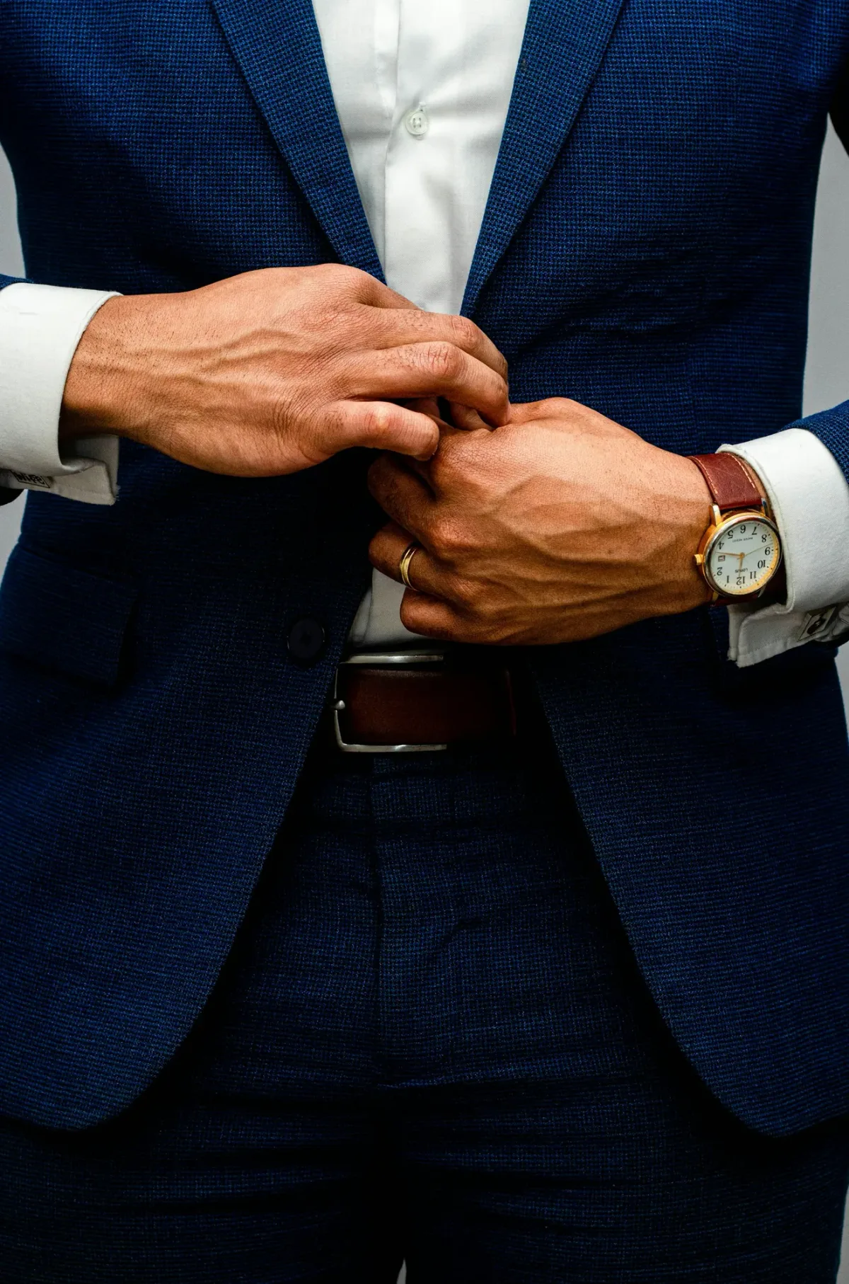 Des mains ferment le bouton d’une veste bleu marine, une montre au poignet